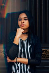 Portrait of young woman with hand on chin standing against wall