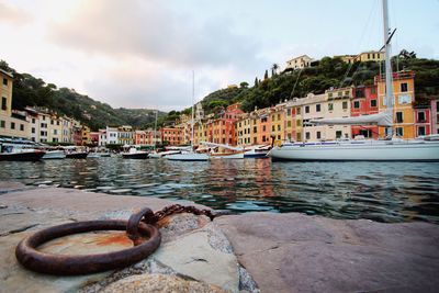 Sailboats moored on harbor by buildings in city against sky