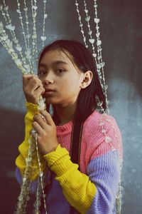 Portrait of girl holding beaded curtain while standing at home