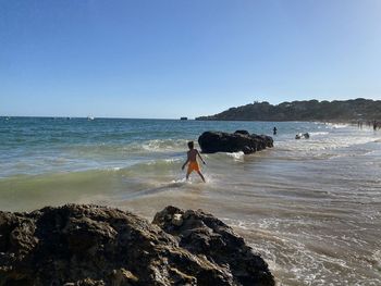 Rear view of boy walking on beach against clear sky