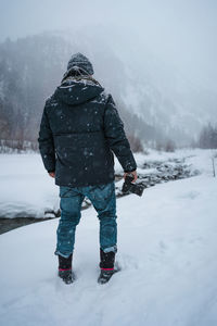 Rear view of man holding camera standing on snow covered land