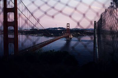 Golden gate bridge over san francisco bay seen through chainlink fence at sunset