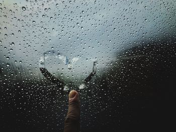 Cropped hand making heart shape on wet window