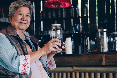 Smiling senior woman holding bottle while sitting at cafe
