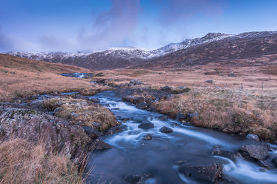 Scenic view of river flowing by mountains against sky