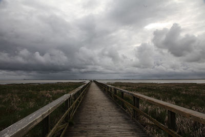 Pier amidst field against cloudy sky