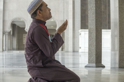 Side view of mature man praying while kneeling at mosque