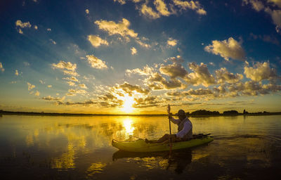 Man kayaking in lake against cloudy sky during sunset