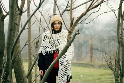 Portrait of young woman standing by trees in winter