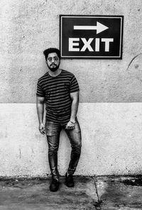 Portrait of young man standing against wall with information sign