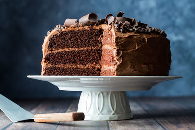 A triple layered homemade chocolate cake on a pedestal stand with slices removed