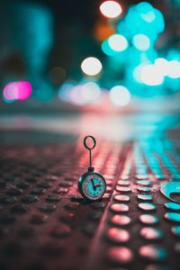 Close-up of pocket watch on footpath in illuminated city at night