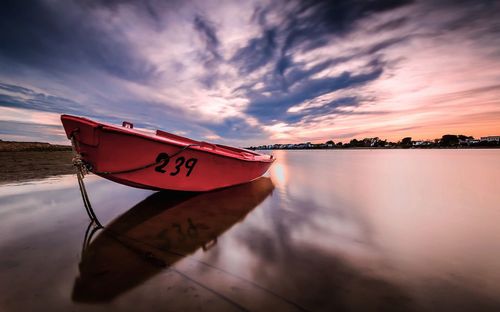 Boat moored at beach against sky during sunset