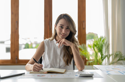 Portrait of young woman using mobile phone while sitting on table