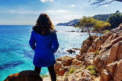 Rear view of woman standing on rock by sea against sky