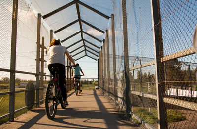 Rear view of people riding bicycles on footpath against sky