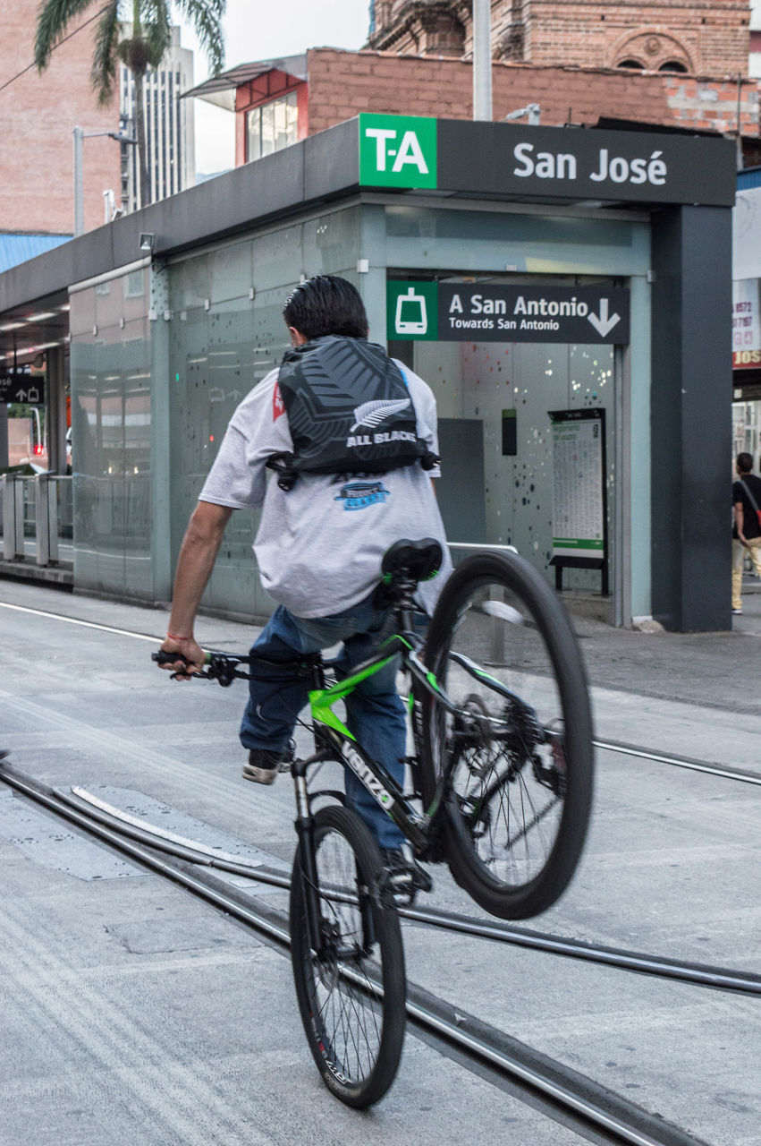 REAR VIEW OF MAN RIDING BICYCLE ON STREET