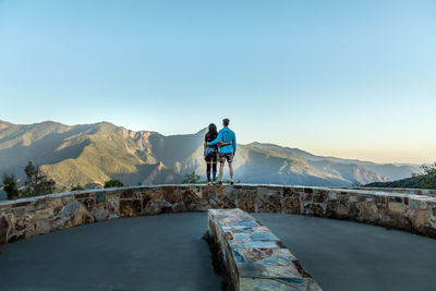 Rear view of couple looking at mountains against clear blue sky