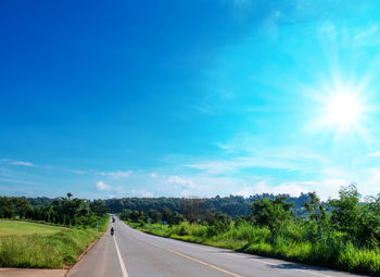 Road by trees against blue sky