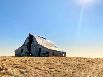 Abandoned building on field against clear blue sky