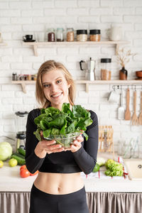 Portrait of smiling young woman holding spinach in kitchen