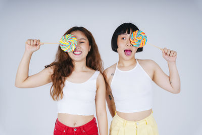 Portrait of lesbian couple holding lollipop against white background