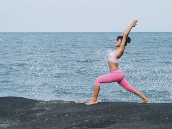 Mature woman exercising on rock by sea