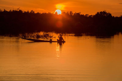 Silhouette man on boat in lake against sky during sunset