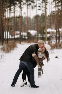 A happy couple in love in winter clothes hugging together walking in a snowy forest on an weekend