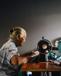 Side view of senior woman stitching using sewing machine at home