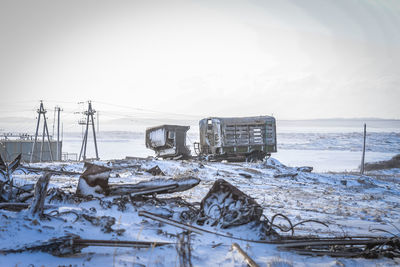 Abandoned vehicles on snow covered field against sky