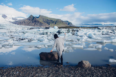 Rear view of woman by rock in front of icebergs