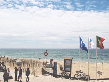 People and flags at beach against sky