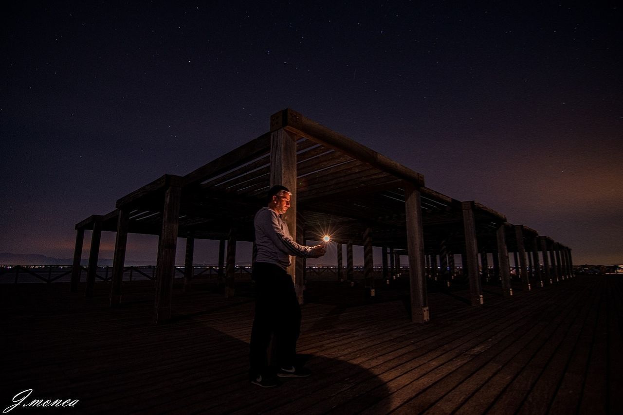 night, star, darkness, sky, one person, astronomy, evening, adult, light, full length, architecture, nature, standing, space, men, arts culture and entertainment, built structure, person, young adult, illuminated, beauty in nature, lifestyles, galaxy, outdoors, dark, wood, long exposure, land, scenics - nature