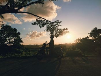 Silhouette people riding bicycle on road against sky during sunset