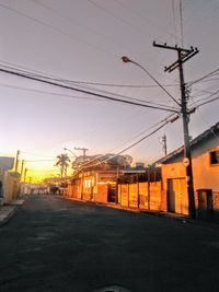 Road by electricity pylon against sky during sunset