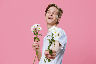 Portrait of young woman with bouquet against pink background