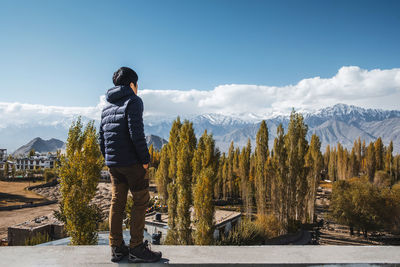 Rear view of woman standing on retaining wall against sky during winter