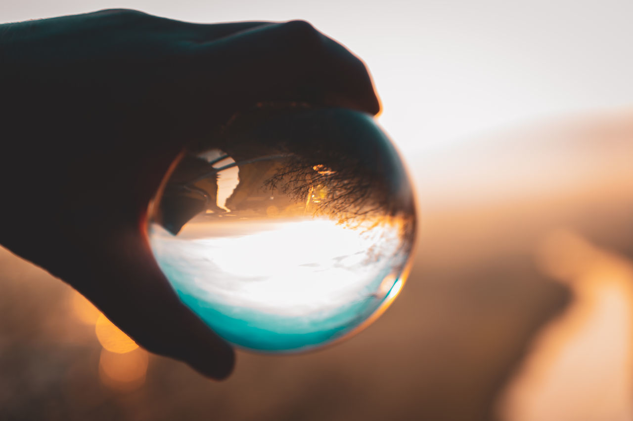 CLOSE-UP OF HAND HOLDING CRYSTAL BALL AGAINST SKY