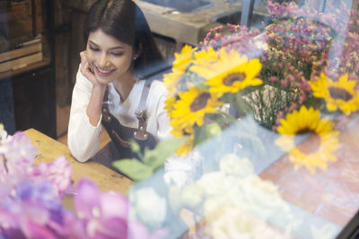 Young woman sitting at flower shop seen through window