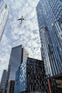 Low angle view of airplane flying above modern buildings