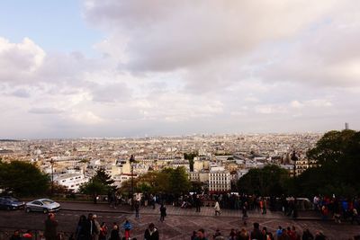 Crowd in city against cloudy sky