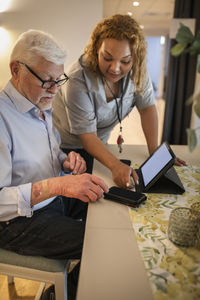 Young female caregiver assisting senior man in using smart phone at retirement home