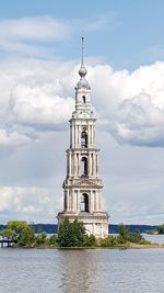 Tower by river against cloudy sky