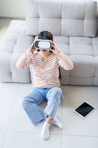 Young asian woman wearing virtual reality glasses sitting on floor at modern home