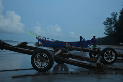 People standing by boat moored at beach against sky