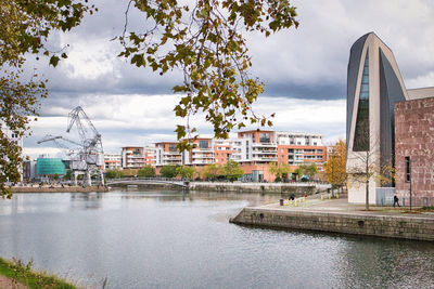 Buildings by river against sky in city