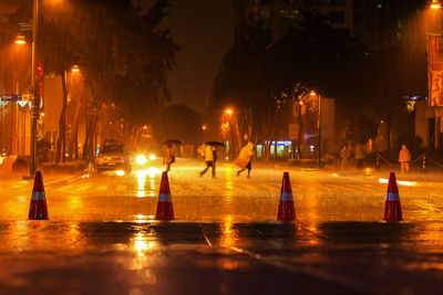 People walking on illuminated city street at night during rain