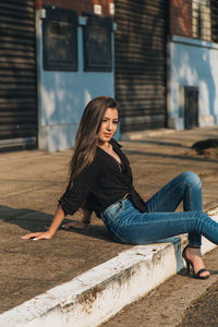 Portrait of young woman sitting on footpath in city