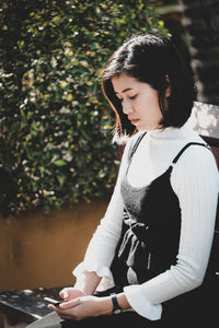 Young woman using mobile phone while sitting on bench